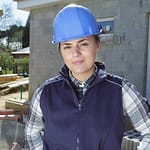 A young woman wearing a construction hat works at a site surrounded by bricks.
